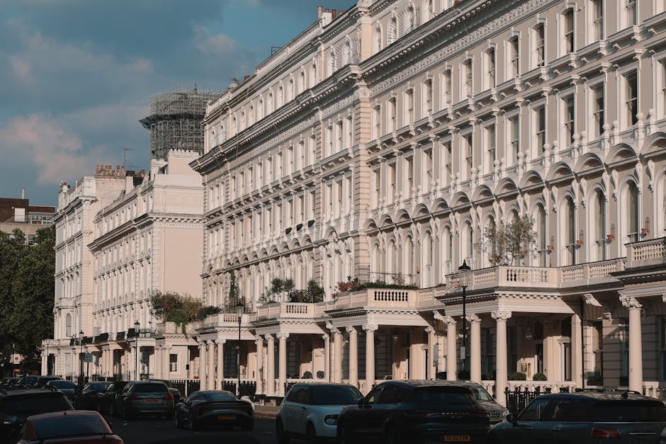 A row of white, multi-story residential buildings with ornate architectural details located on Westbourne Terrace, captured during daylight hours with clear blue sky. The buildings feature large sash